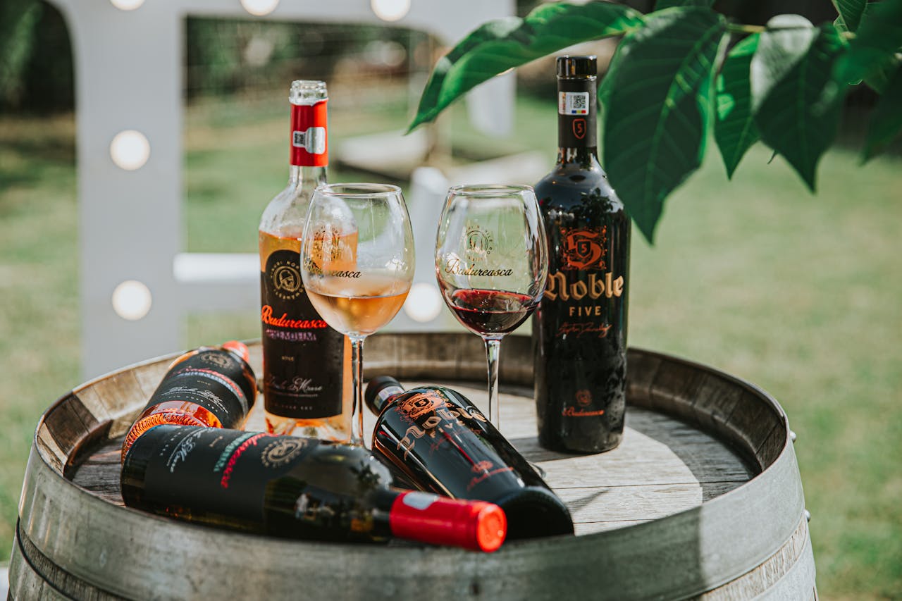 Home Rustic display of bottled wines and glasses on a wooden barrel in an outdoor setting.