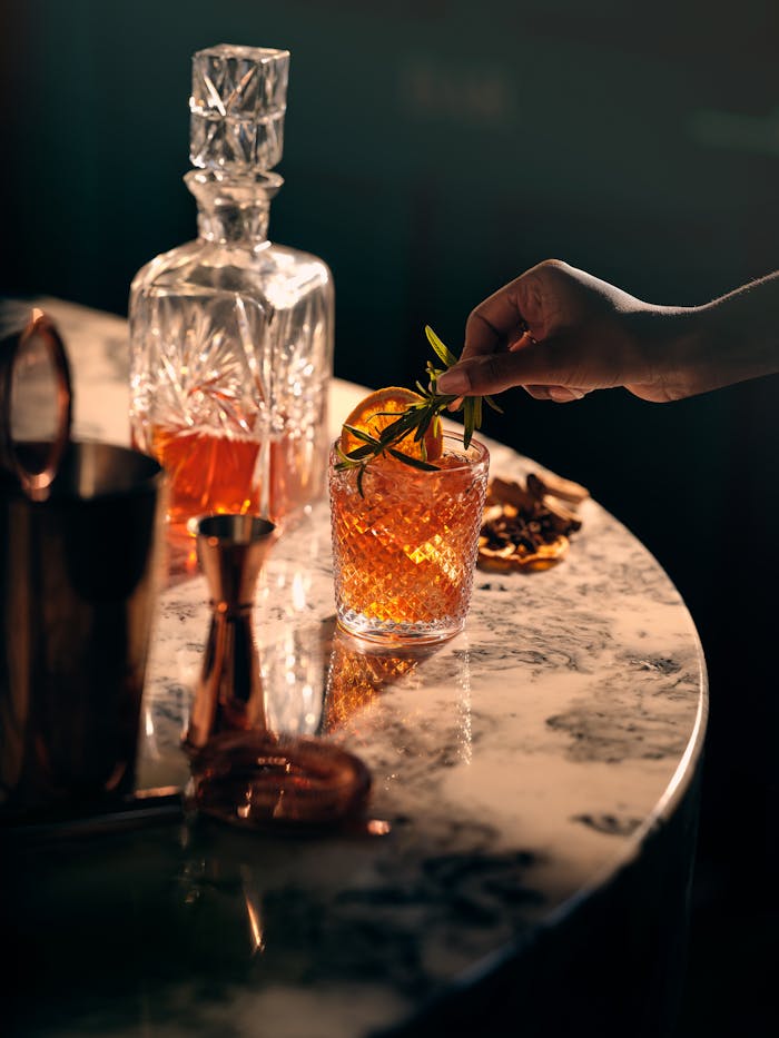 About A stylish setup showcasing a hand garnishing a whiskey cocktail on a marble table.