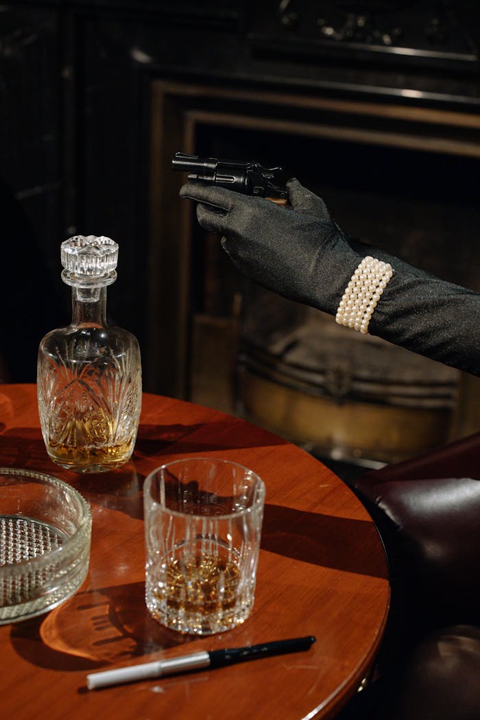 Cinematic noir scene featuring a gloved hand with a gun and a whiskey setup.