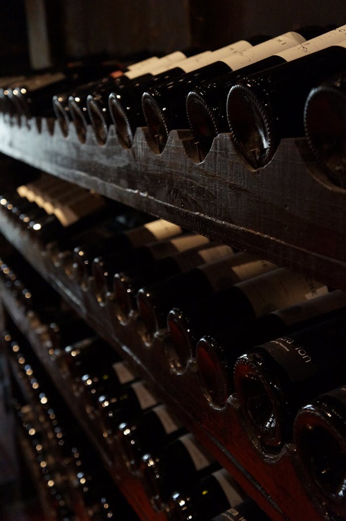 Home A dimly lit wine cellar showcasing rows of wine bottles on rustic wooden shelves, creating a classic and elegant atmosphere.